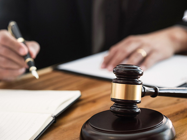 Close-up of a judge's gavel on a desk with a person signing a document in the background
