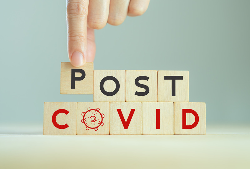 Wooden letter tiles spelling POST COVID with COVID in red letters on a light blue background