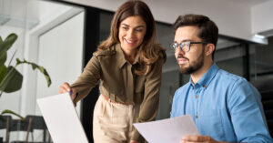 Women pointing at screen and male holding paper looking at screen