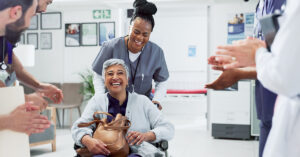 Hospital staff member pushing a patient in a wheelchair through a line of hospital staff that are cheering.