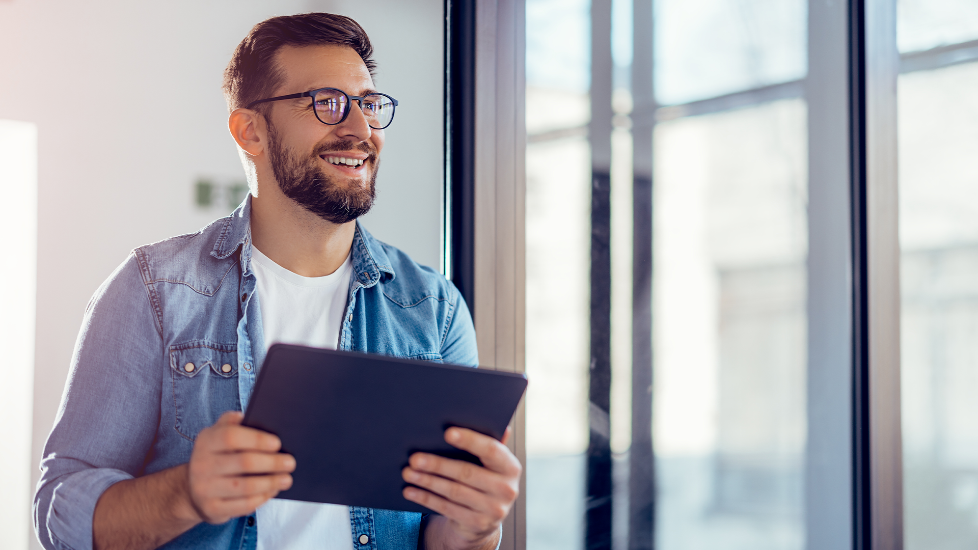 Man holding a tablet looking out the window smiling