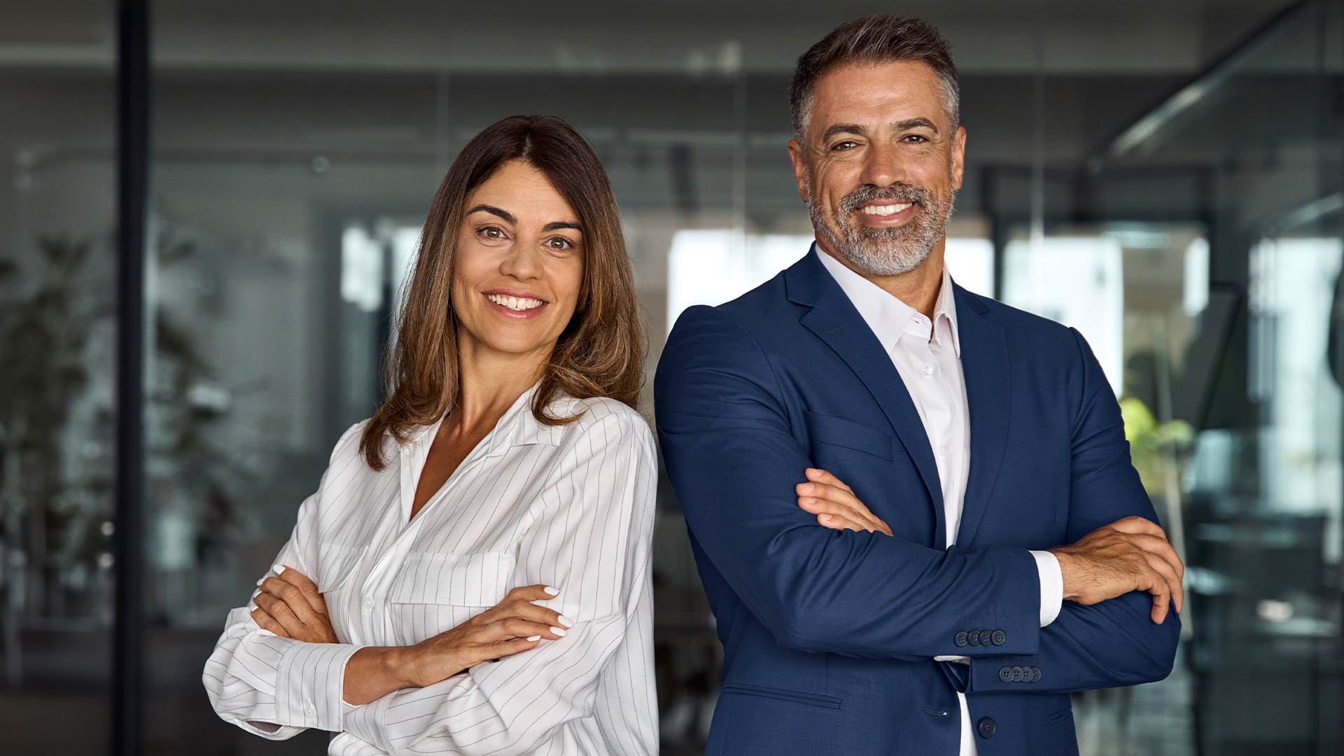 Man and woman posing back-to-back wearing business professional clothing in an office setting