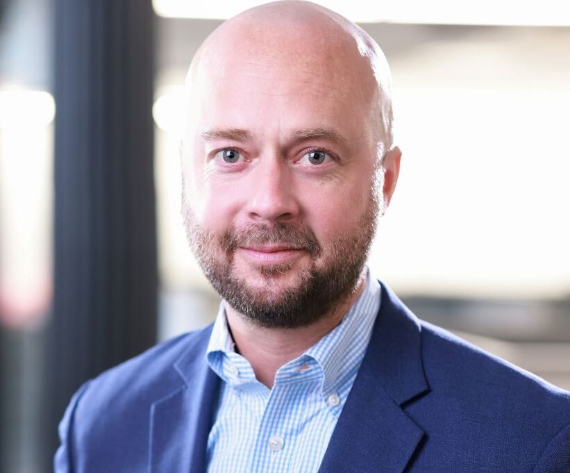 Professional headshot of a bald man with a beard wearing a blue suit jacket