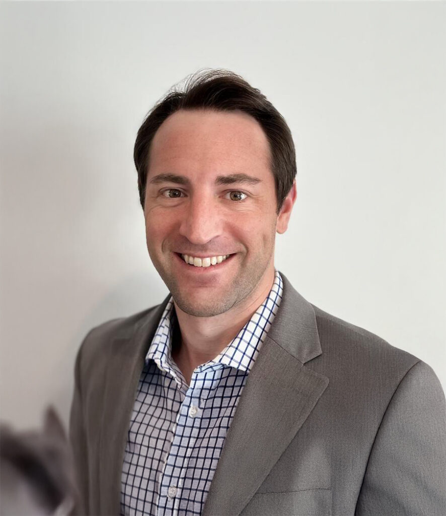 Professional headshot of a man in a gray blazer over a checkered shirt