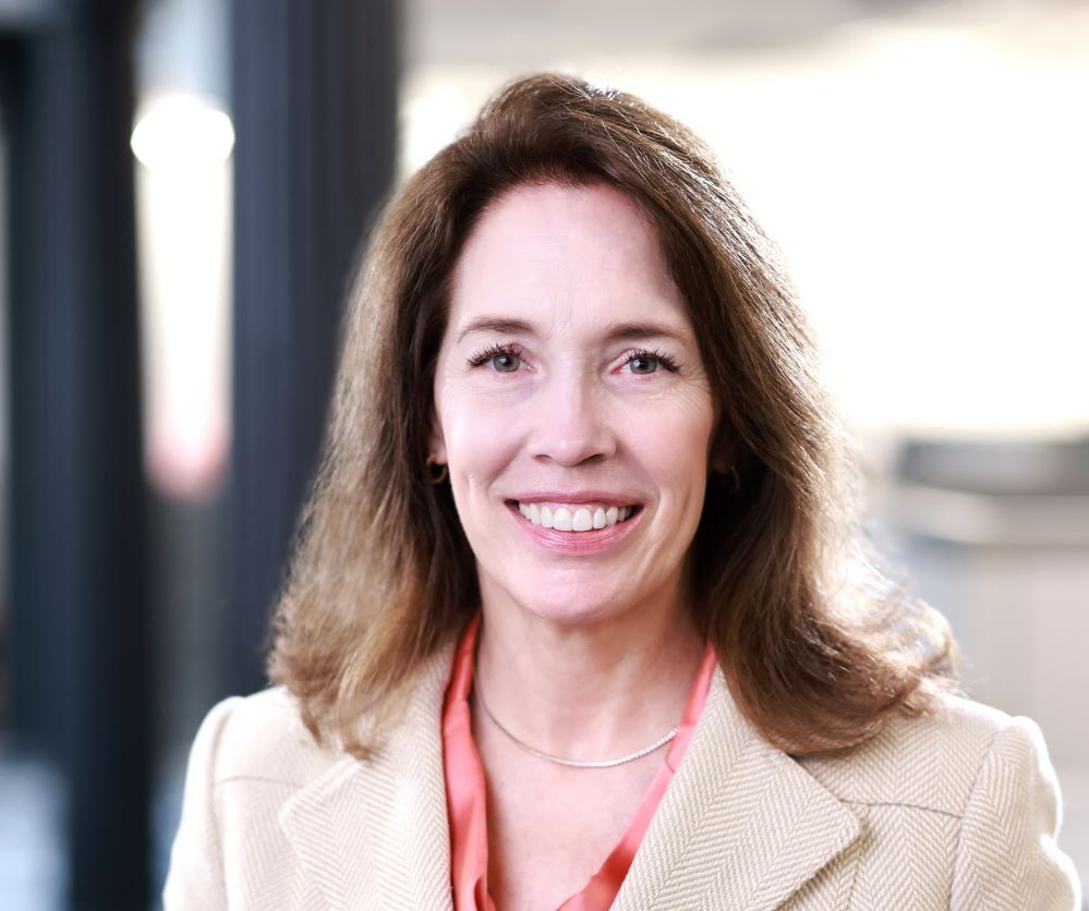 Professional headshot of a woman with medium brown hair in a salmon blazer
