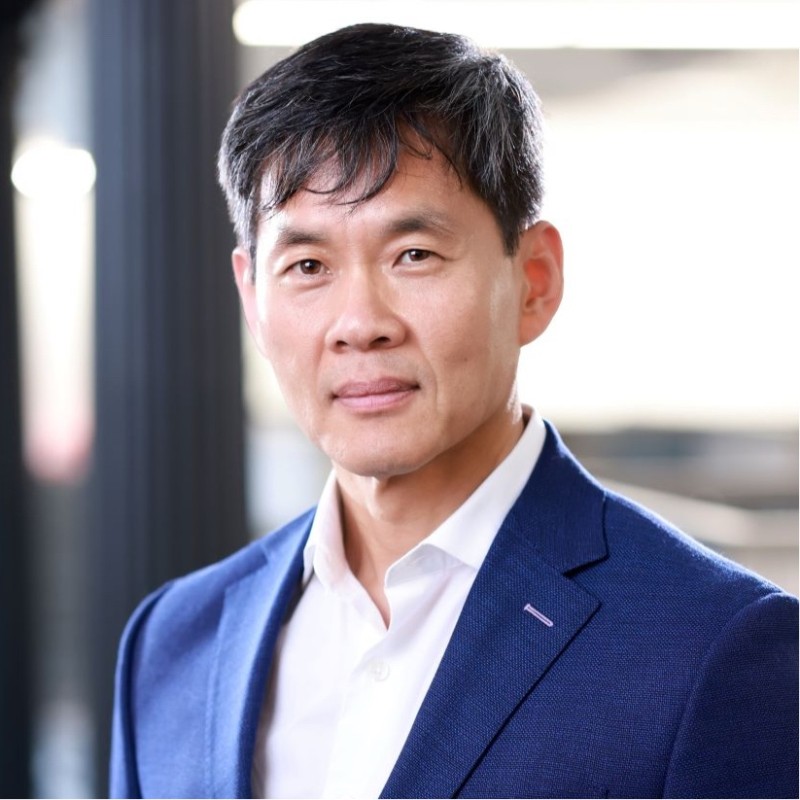 Professional headshot of an Asian man in a blue blazer against a dark background