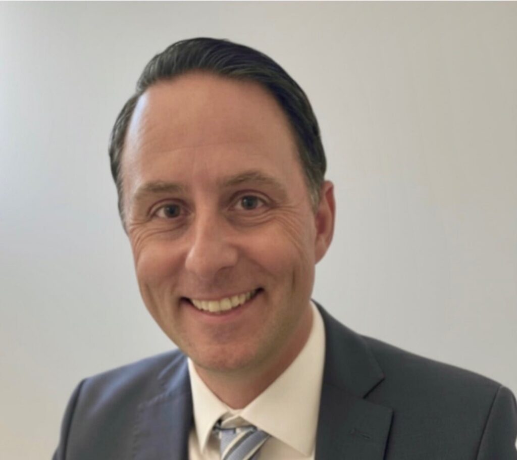 Professional headshot of a man with short dark hair in a suit and tie