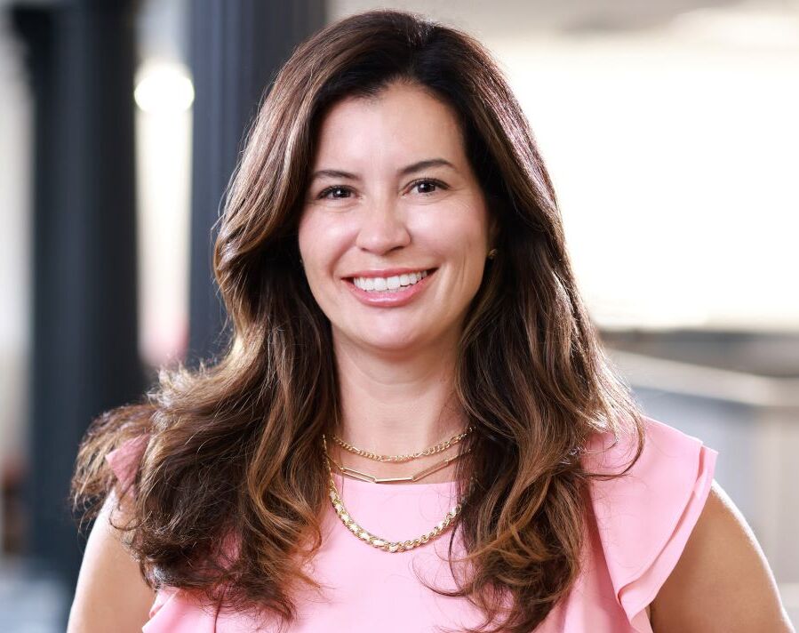 Professional headshot of a smiling woman with long brown wavy hair in a pink top