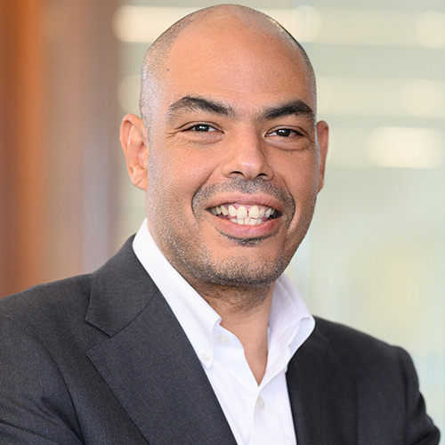 Professional headshot of a man with a shaved head in a white dress shirt