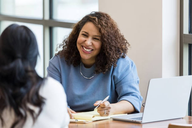Two women smiling and collaborating over a laptop in a bright office