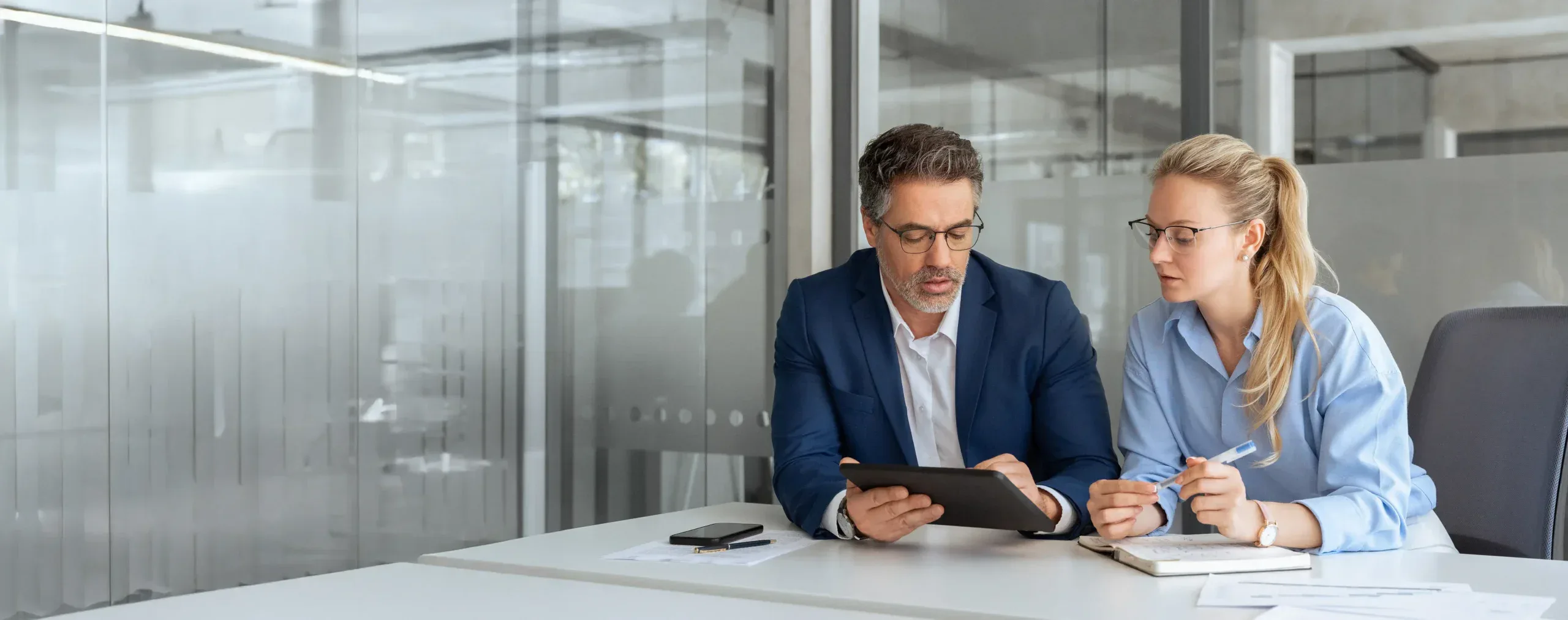 Man with a beard and glasses looking at and engaging with a tablet he holds